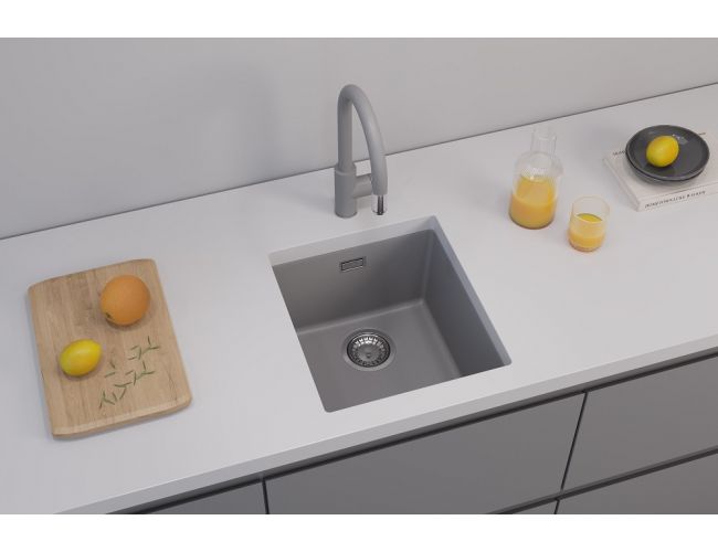 Sivo, granitno vgradno pomivalno korito s sivo kuhinjsko armaturo na beli delovni površini z leseno desko za rezanje in korazcem s sokom zraven